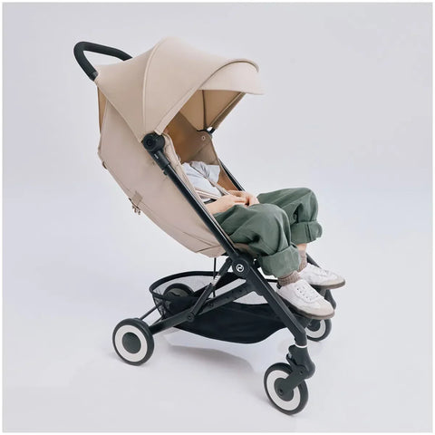 Almond Beige CYBEX Agis baby stroller with a child sitting inside in front of a light gray background