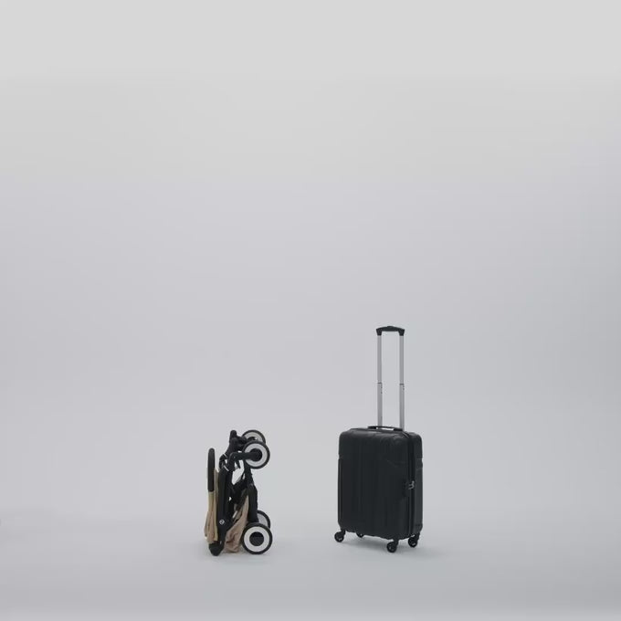 Short video starting with a folder cybex agis stroller and a black travel suitcase in front of a white background. A man comes in the frame, grabs both with ease and walks out of the frame.