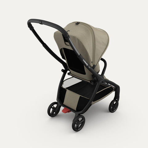 Rear view of the taupe-colored Redsbaby Aeron stroller with a black frame. The stroller features a large canopy, mesh back panel for ventilation, spacious storage basket underneath, and no-puncture wheels with a red brake pedal on the rear wheels. The sleek and modern design highlights its practicality and functionality.